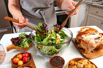 Chef prepares caesar salad with vegetables and chicken in home kitchen. Croutons, chicken and salt in the foreground.