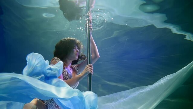 attractive woman diving inside swimming pool, fashion model or dancer posing near pylon in water