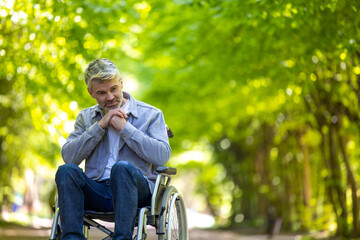 Disable man wearing casual clothing spending time in summer park riding wheelchair.