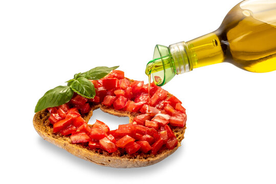 Italian dry bread friselle with chopped cherry tomatoes and basil leaves dressed with olive oil poured from oil bottle - isolated