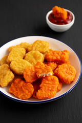Homemade Spicy Chicken Nuggets Mix on black background, side view.
