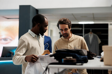 Fashion boutique employee assisting african american customer in choosing formal outfit. Clothing store client getting help from showroom worker while selecting shirt size