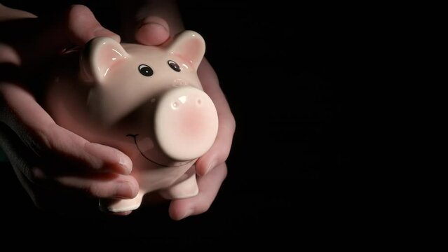 Hand hold piggy bank on black background. A view of woman hands hola the piggy bank on the black background. A concept of save money for family.