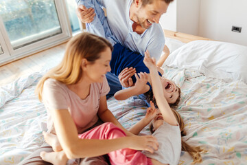 Young family playing on the bed in the bedroom while wearing pajamas at home