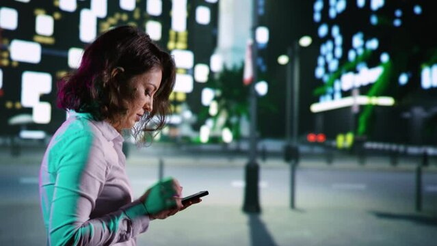 Adult on smartphone walking near city center, looking at maps for directions on night promenade. Woman relaxing with evening stroll reading texts, looking at skyscrapers downtown. Handheld shot.