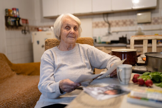 One woman senior grandmother pensioner female with dementia alzheimer's disease and depression sitting at table at home alone hold and watch photos real people copy space