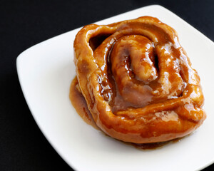 Freshly baked caramel roll on a white plate in a black background 