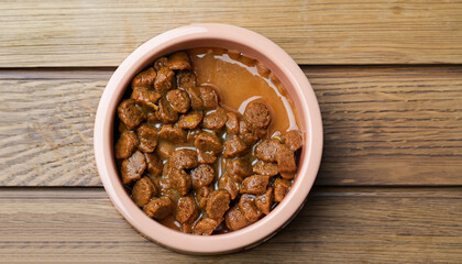 Wet pet food in feeding bowl on wooden table, top view