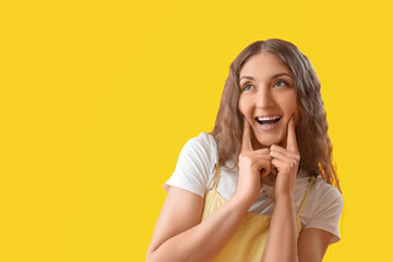 Happy young woman touching her cheeks on yellow background