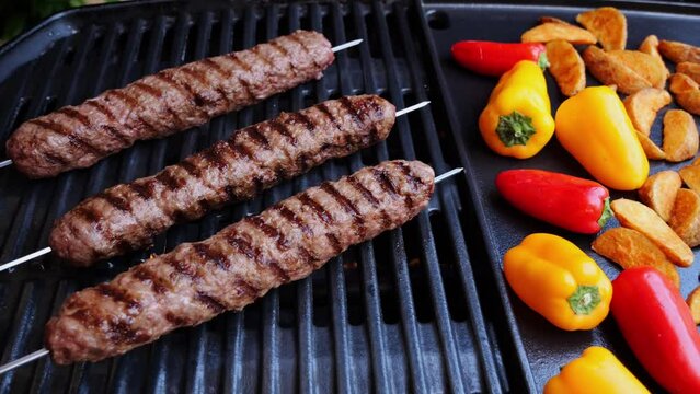 Grilled Lula kebab on skewer on grill, barbecue, potatoes wedges, sweet pepper, hot cast iron grate. Close up.