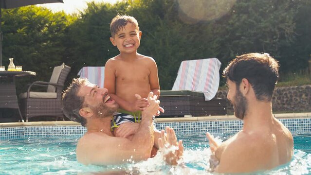 Same sex family with two Dads having fun with son in swimming pool on summer holiday - shot in slow motion