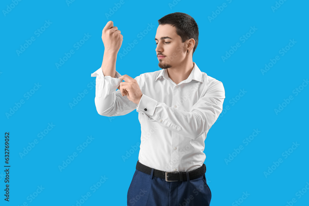 Wall mural Young businessman rolling up his sleeve on light blue background