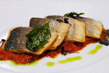 mediterranean pan seared sea bass fish fillet with tomato saffron sauce and basil in a white plate
