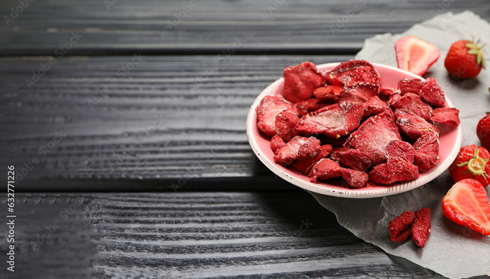 Wall mural Freeze dried and fresh strawberries on black wooden table. Space for text