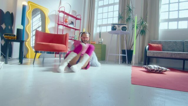 Eccentric queer dancer with beard and pigtails wearing girly outfit voguing in trendy studio and posing for camera. Zoom handheld shot