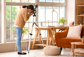 Young Asian woman using telescope at home