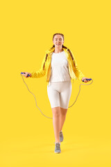 Sporty young woman jumping with rope on yellow background