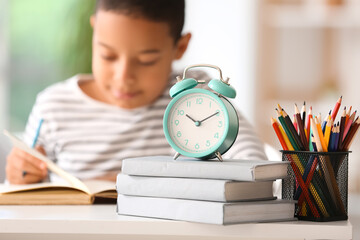Alarm clock with books and pen cup on table of little boy doing lessons at home, closeup - Powered by Adobe