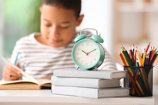Alarm clock with books and pen cup on table of little boy doing lessons at home, closeup