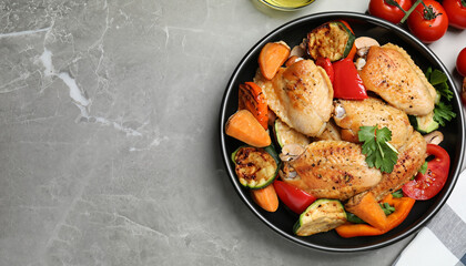Delicious cooked chicken and vegetables on grey marble table, flat lay with space for text. Healthy...
