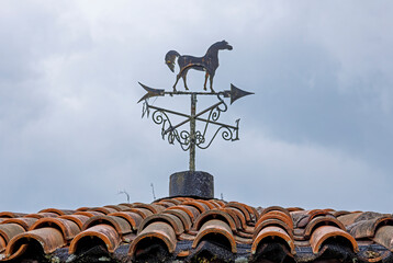A horse figure above a compass rose in al old weather vane on a roof top, riding through the wind...