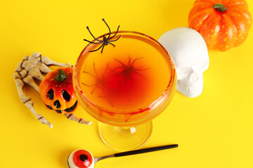 Glass of tasty Margarita cocktail, skull, skeleton hand and pumpkins for Halloween on yellow background