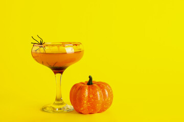 Glass of tasty Margarita cocktail and pumpkin for Halloween on yellow background