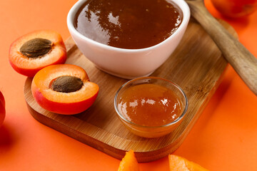 Wooden board with bowls of sweet apricot jam on orange background