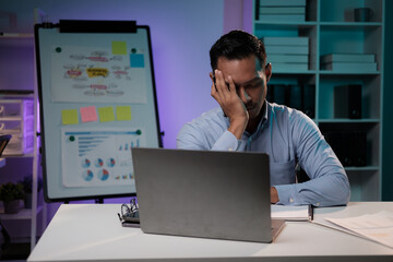Tired and exhausted young Asian businessman feeling upset and tired after working too much, working over night alone in his office room.