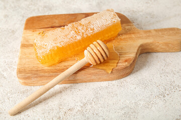 Wooden board with fresh honeycomb and dipper on light background
