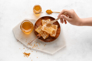 Woman pouring sweet honey onto combs on white background