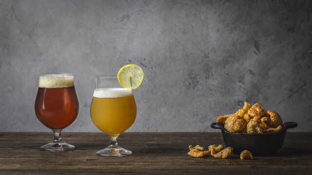 One Wheat and one brown ale, in Tulip glasses on wood table with bowl of pork rinds