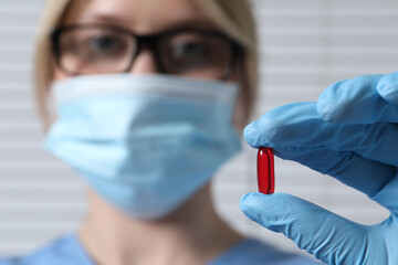 Doctor holding pill on light background, selective focus. Space for text