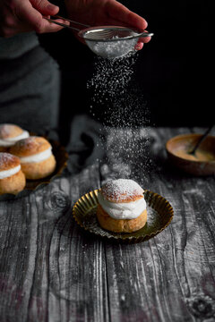 Semlor Buns on Wood Backdrop with icing sugar on tray with hands