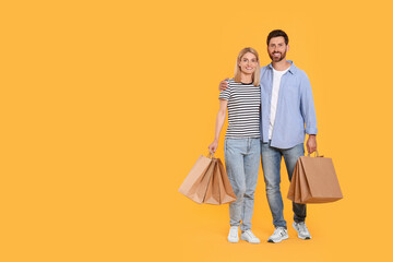 Family shopping. Happy couple with paper bags on orange background. Space for text