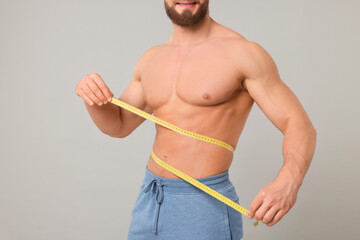 Athletic man measuring waist with tape on light grey background, closeup. Weight loss concept - obrazy, fototapety, plakaty