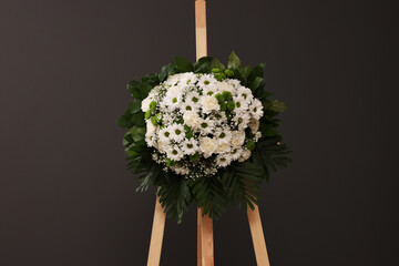 Funeral wreath of flowers on wooden stand against grey background