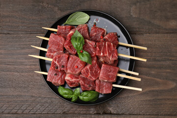 Skewers with cut fresh beef meat, basil leaves and spices on wooden table, top view
