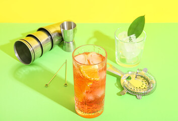 Glass of cold Negroni cocktail, ice cubes and bartender tools on color background