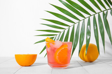 Glass of cold Negroni cocktail, oranges and palm leaf on light tile table