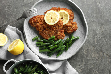 Tasty schnitzels served with lemon and green beans on grey table, flat lay