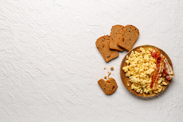 Plate of tasty scrambled eggs with bacon on white background