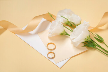Wedding rings, card, ribbon and eustoma flowers on color background