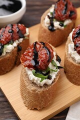 Delicious bruschettas with sun-dried tomatoes, cream cheese and balsamic vinegar on table, closeup