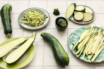 Plates with slices of fresh green zucchini on white tile background
