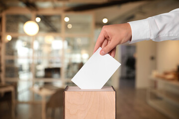 Man putting his vote into ballot box on blurred background, closeup