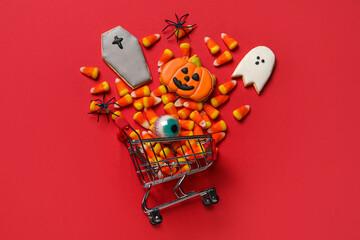 Shopping cart with tasty candy corns and cookies for Halloween on red background
