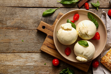 Plate of tasty Burrata cheese with basil and tomatoes on wooden background