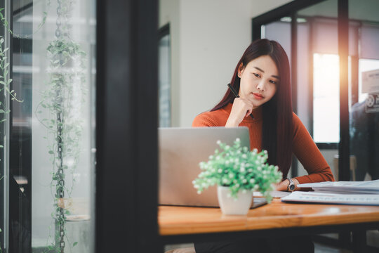 Beautiful Asian woman using laptop and tablet while sitting at her working place. Concentrated at work.