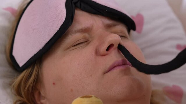 Portrait of sleeping woman in sleep mask, pet shakes its tail, puts it in nose, tickles. Allergy to animal fur, advertisement for sleeping pills for sound sleep. Lonely spinster concept with cats, dog